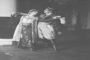 Schwarzes und weißes Foto eines Mannes und einer Frau, die in einem Ballsaal tanzen, mit einer Säule und einer Wand im Hintergrund; der Mann trägt Schuhe, was darauf hinweist, dass sie eine Vorstellung geben.