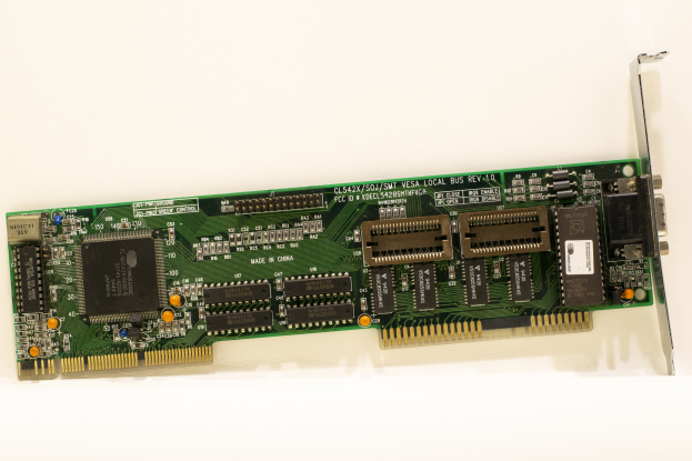 Nahaufnahme einer PCI-E-Karte auf einer weißen Oberfläche mit einem zentralen Chip und mehreren angeschlossenen Verbindern.