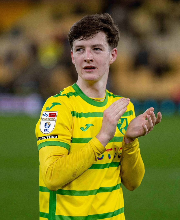 Ein junger Mann in einem gelb-grünen T-Shirt klatscht auf einem Fußballfeld in die Hände, der Hintergrund ist unscharf.