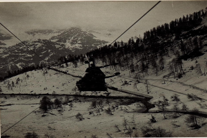 Schwarze-Weiß-Foto einer Person auf einem Skilift mit schneebedeckten Bergen und Bäumen im Hintergrund, mit Text unten.