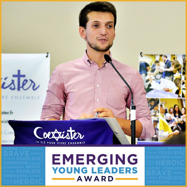 Ein Mann steht an einem Podium mit einem Mikrofon, haltend ein Blatt Papier, vor einer Tafel mit der Aufschrift "Emerging Young Leaders Award", mit mehreren Personen rechts von ihm.