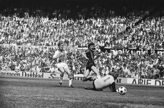 Schwarz-weiß-Foto von Männern, die auf einem Feld Fußball spielen, mit Zuschauern im Hintergrund und einer 'Bundesliga 1978-79 Ajax 1-1 Hannover 96'-Tafel.