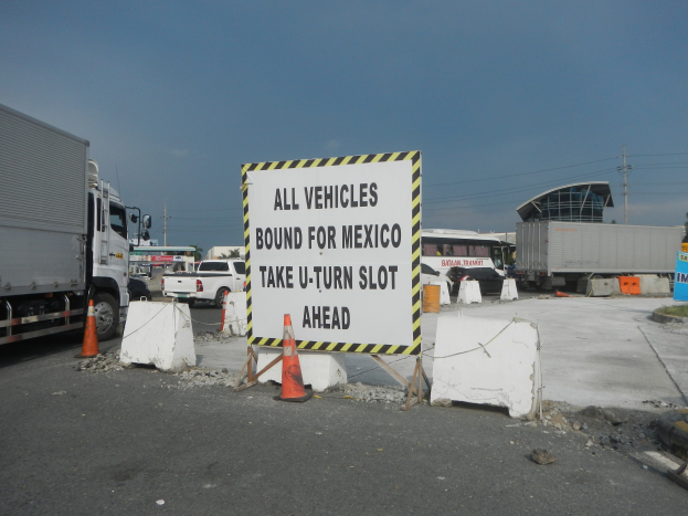 Ein Lastwagen auf einem Parkplatz neben einem Schild mit der Aufschrift "Alle Fahrzeuge nach Mexiko" mit verstreuten Verkehrskegeln, Brettern und Hintergrundgebäuden, Bäumen, Polen und einem klaren Himmel.