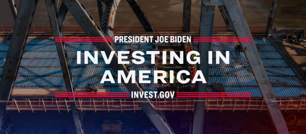 Präsident Joe Biden steht neben einer Brücke mit dem Text "Investing in America" und verstreuten Gegenständen im Vordergrund.