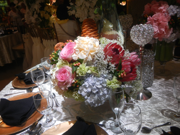 Ein formeller Esstisch mit Tellern, Besteck, Gläsern, Servietten und Blumenvasen, mit einem Blumenstrauß in der Mitte und Stühlen im Hintergrund.